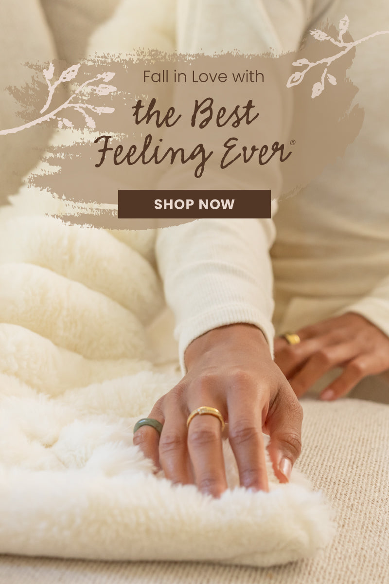 A cozy lifestyle shot of a person wearing a cream ribbed long-sleeve top and touching a fluffy cream throw blanket. The image features a warm beige graphic overlay with white leaf illustrations and the text 'Fall in Love with the Best Feeling Ever' and a 'SHOP NOW' button.