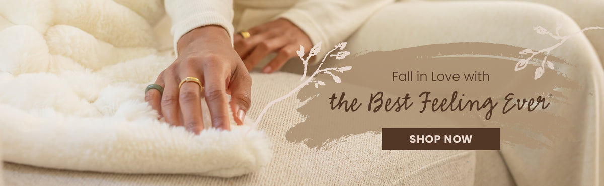 A close-up lifestyle shot of a person resting their hands on a soft, fluffy cream-colored blanket or throw. The background shows a matching beige textured surface, likely a sofa or chair.

