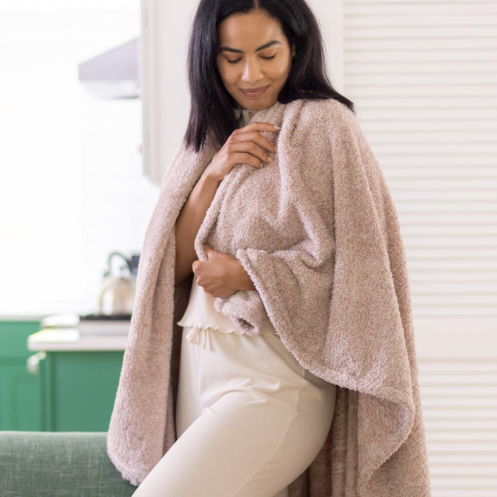 A woman in white standing in a room with our Hushed Auburn Retro Comfort Plush Throw draped over her shoulders as she smiles softly.