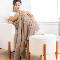 A woman sitting on a white chair with a brown throw over her legs.