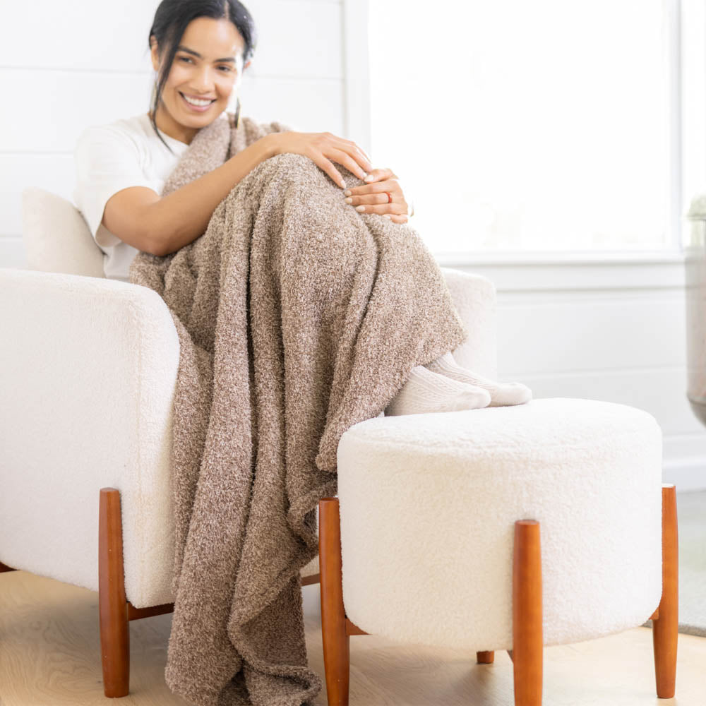 A woman sitting on a white chair with a brown throw over her legs.