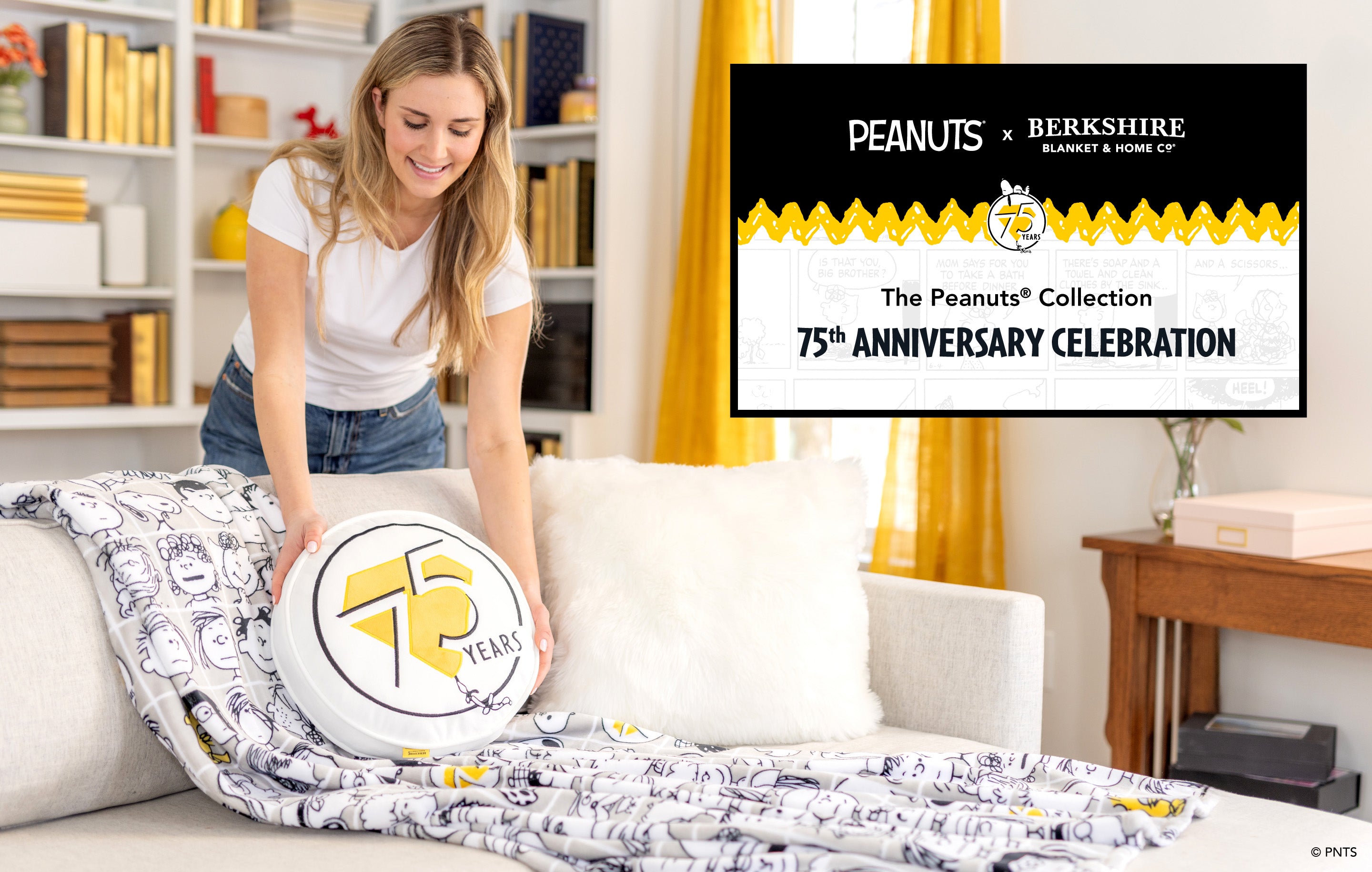 The Peanuts® Collection. 75th Anniversary Celebration. Image of a girl with a throw and pillow set, in a room that is black, white, and gold themed. 