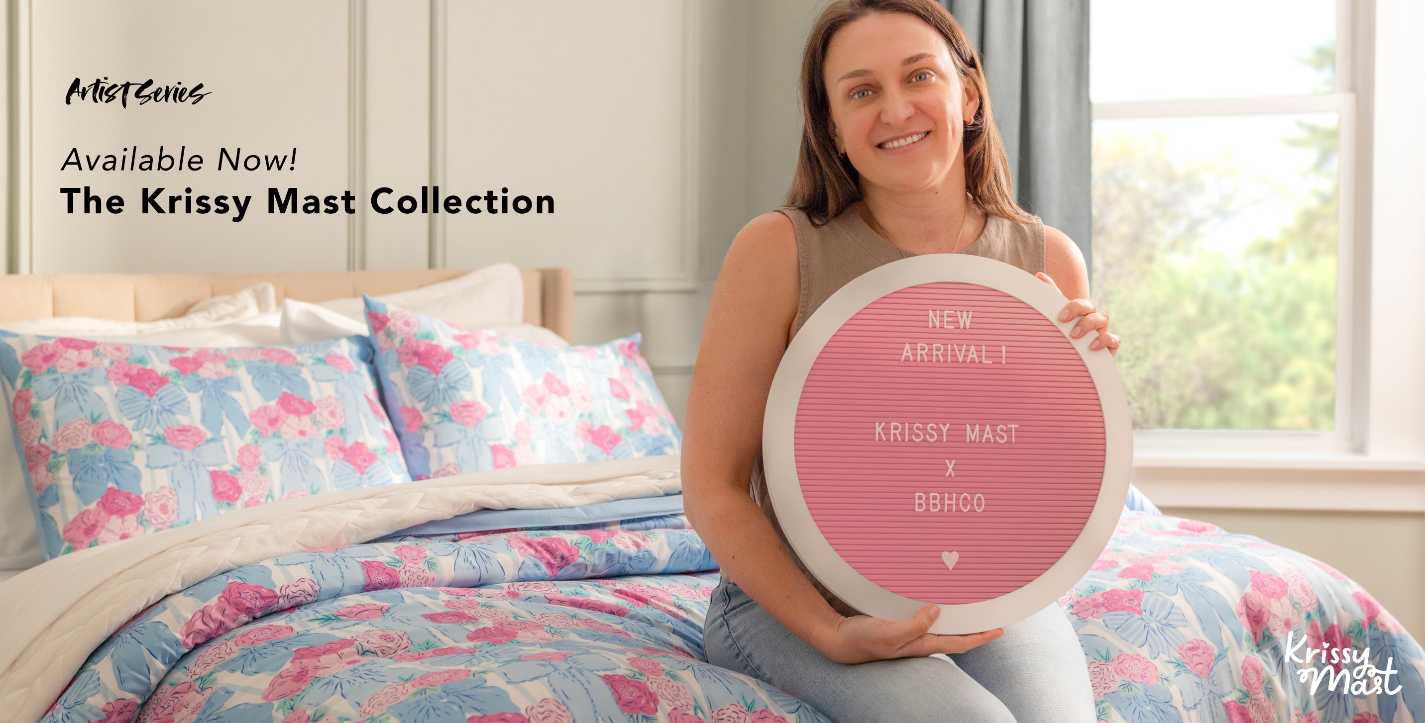 Say Hello to the Krissy Mast Collection! Shop Now! Image of artist, Krissy Mast, sitting on the foot of a bed that is styled with her product collection.