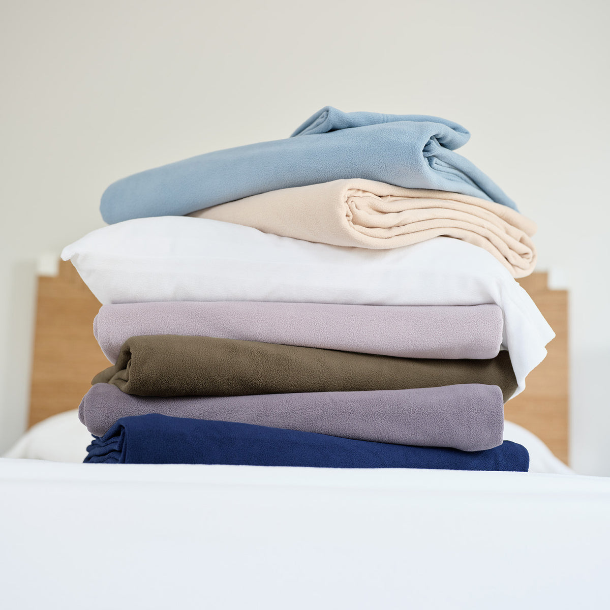 All-Season Microfleece Sheet Sets folded in a stack of assorted Colors on a bed