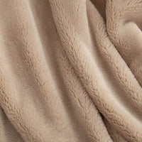 A close-up of a soft, plush fleece blanket in a warm beige color, draped in gentle folds to show its texture.