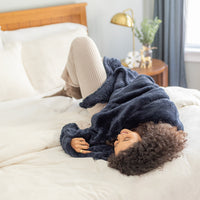 Person lying on a bed wrapped in a navy blue blanket in a cozy bedroom setting.