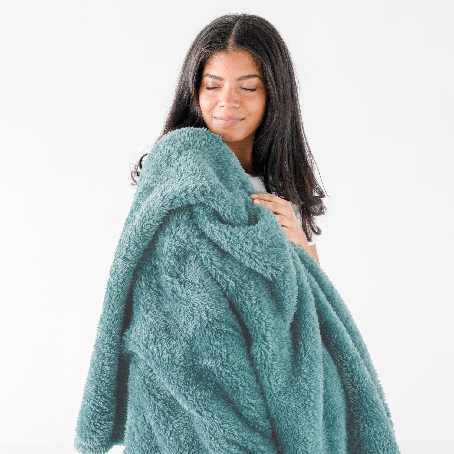 A woman with long dark hair is wrapped in a plush, textured teal fleece blanket against a clean white background.
