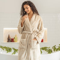 Woman wearing a beige robe in a bathroom setting with decorative elements.