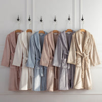 A row of VelvetLoft Robes in assorted colors hanging on wooden hooks against a white wall.