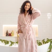 Woman wearing a pink robe in a bathroom setting with decorative elements.