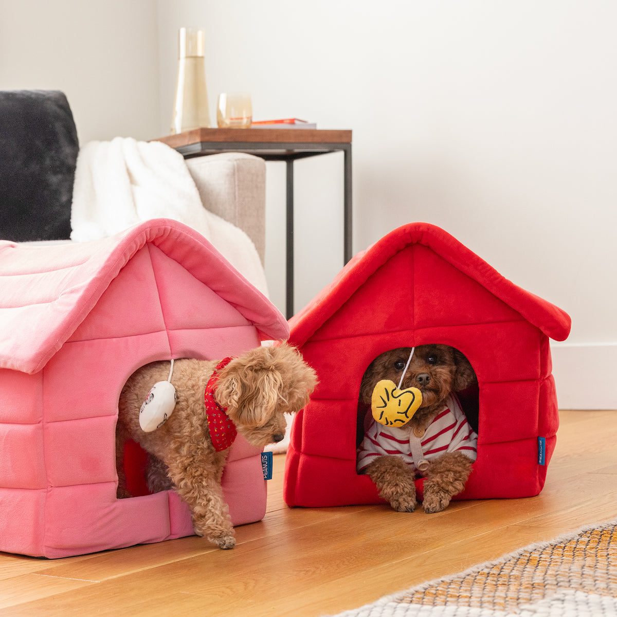 Two dogs sitting inside of pink and red snoopy dog houses in a living room.