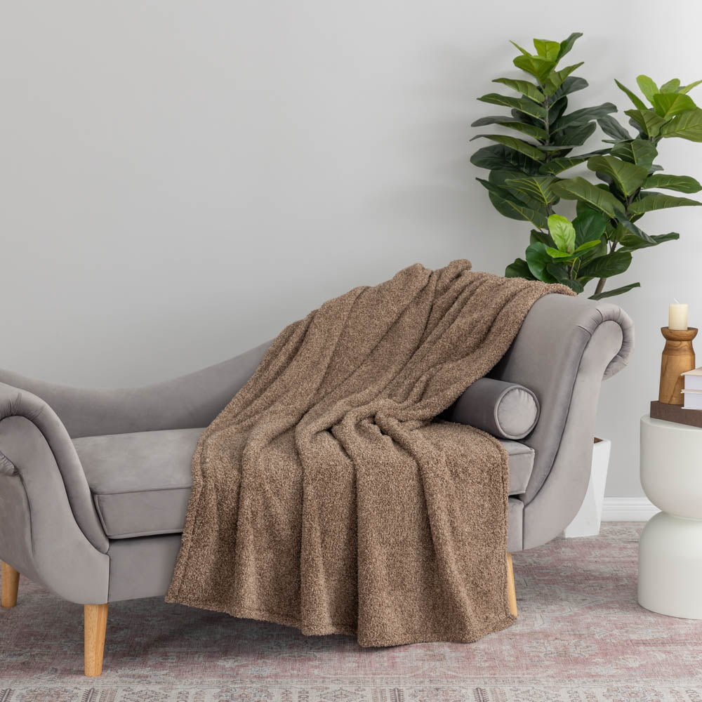 Brown blanket draped over a gray armchair in a living room with a plant and candle holder.