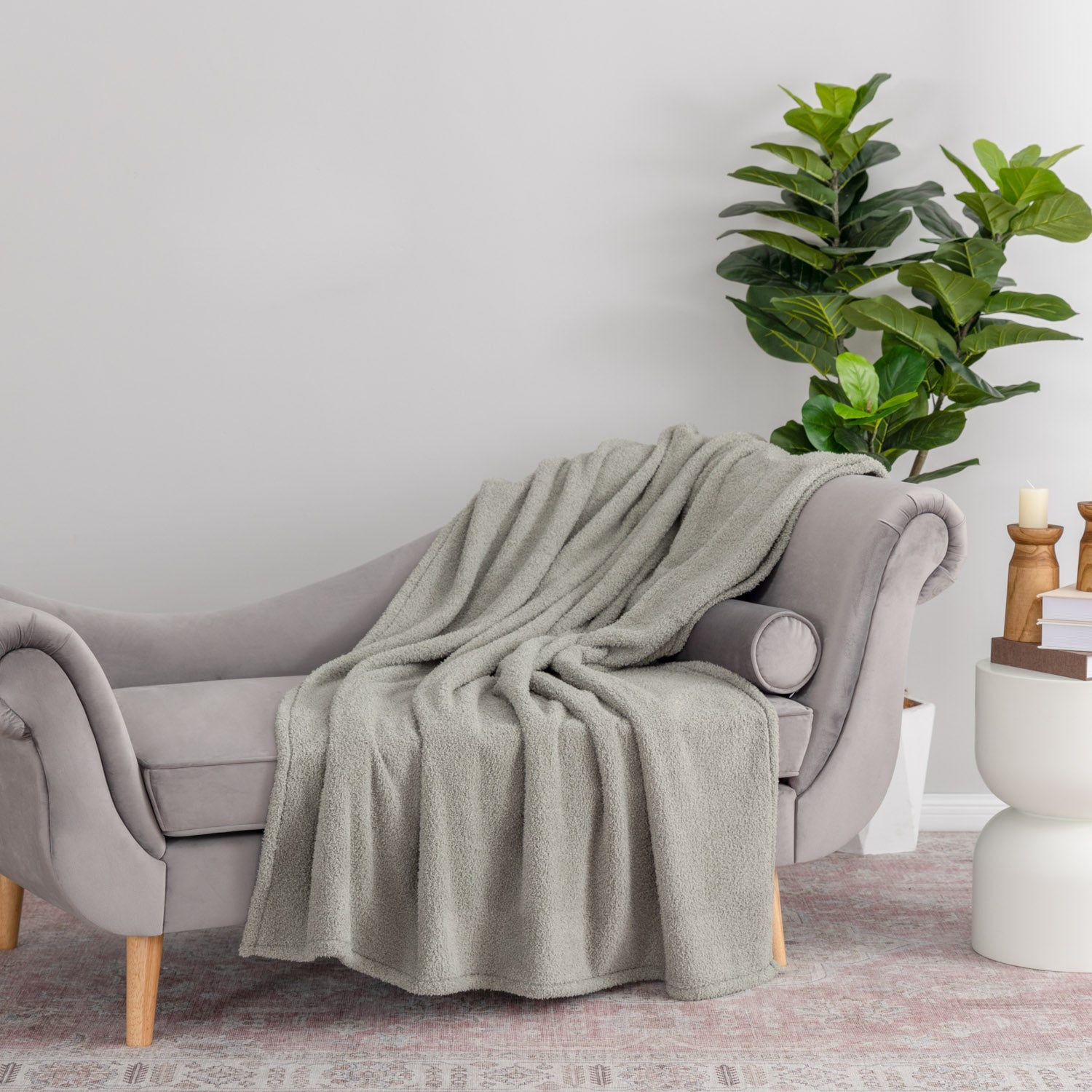 Green blanket draped over a gray sofa in a room with a plant and candle holder.