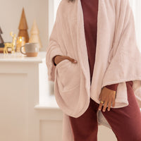 Person wearing a light pink cape wrap with a blurred background