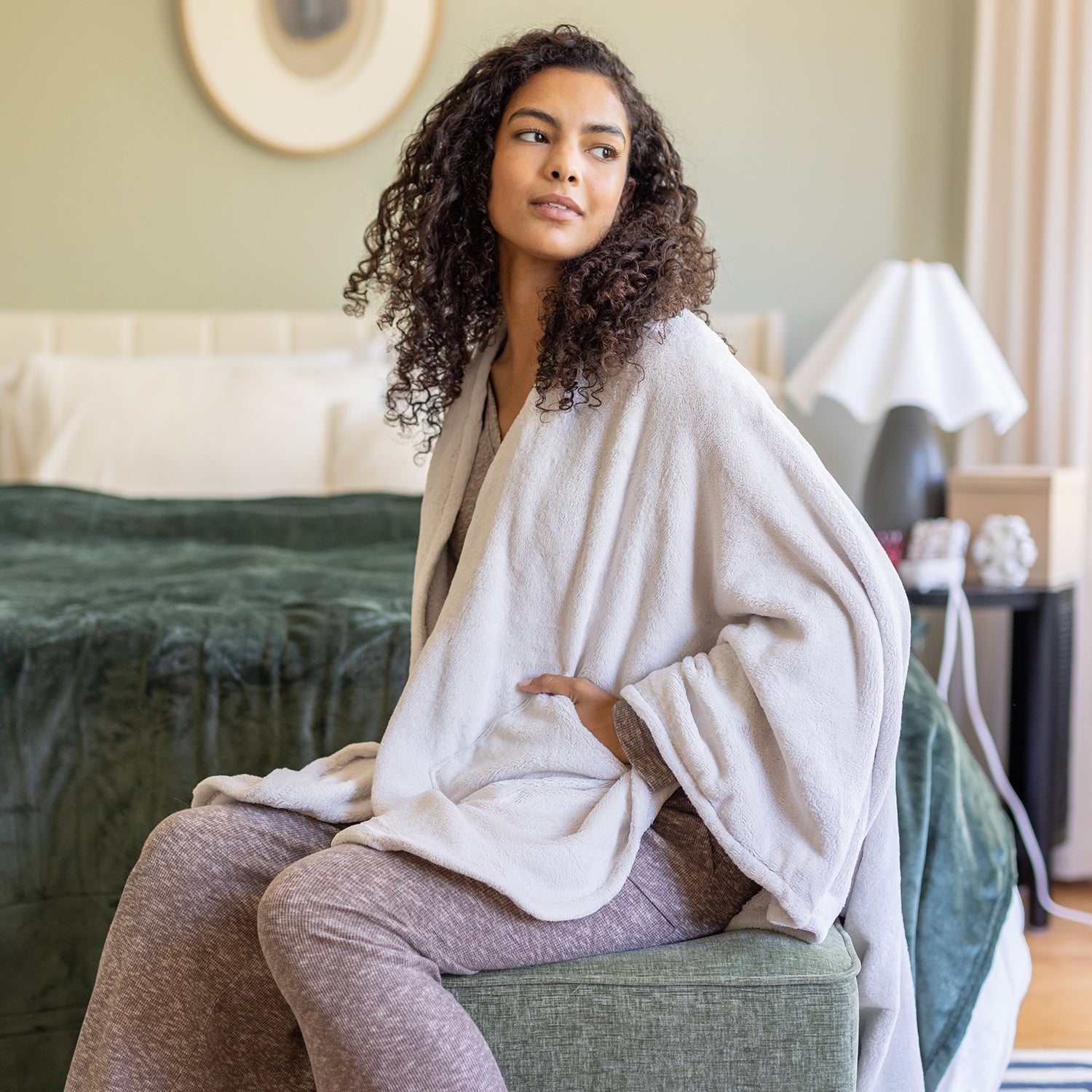 Woman sitting on a bed wearing a white cape wrap in a bedroom setting