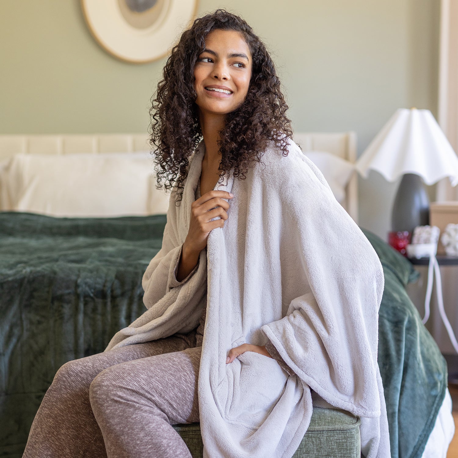 Woman sitting on a couch wrapped in a cape wrap in a cozy living room setting.