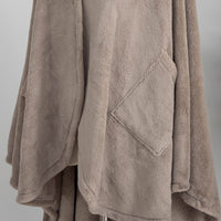 A taupe PrimaLush Cape Wrap displayed on a mannequin in a bright, modern room.