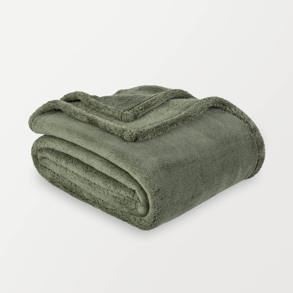 A green fluffy blanket folded neatly on a white surface.