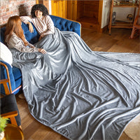 2 people sitting under a grey velvety plush family blanket as they conversate in a living room.