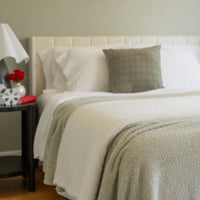 Neatly made bed with white bedding and a green throw blanket in a bedroom setting.