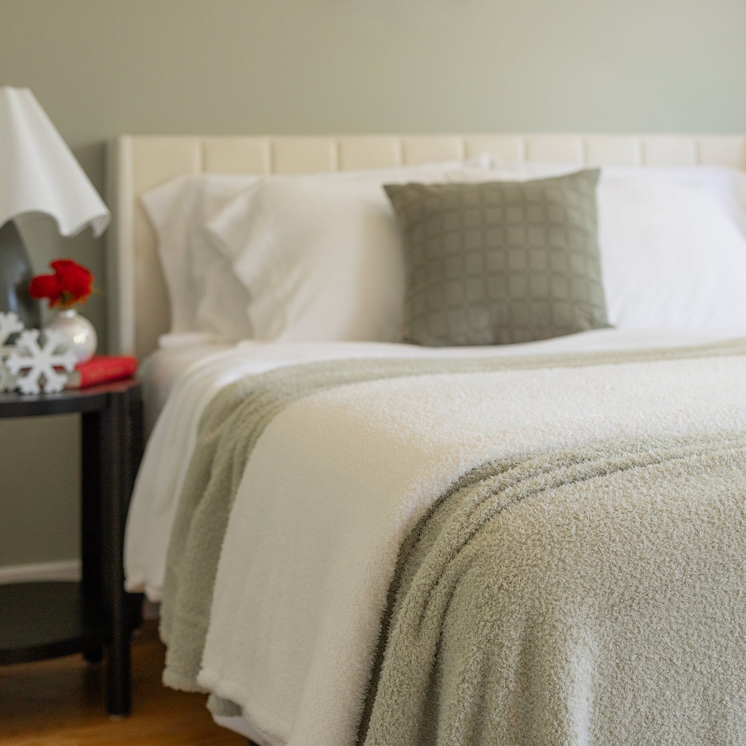 Neatly made bed with white bedding and a green throw blanket in a bedroom setting.