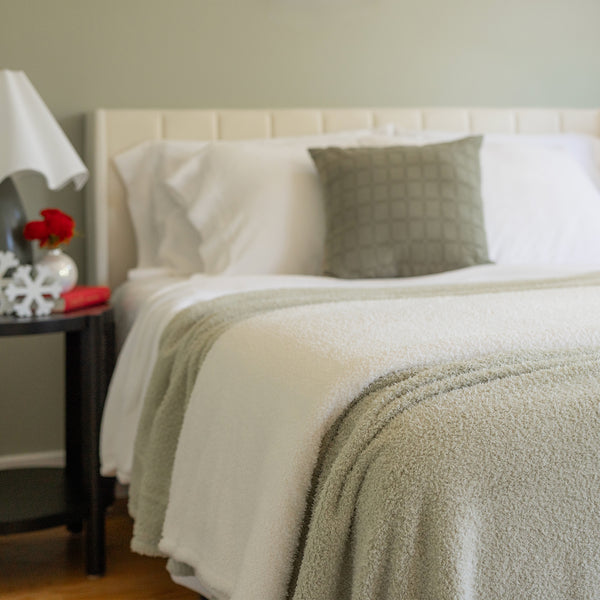 Neatly made bed with white bedding and a green throw blanket in a bedroom setting.