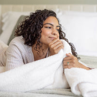 Woman lying in bed with a blanket, looking thoughtful.