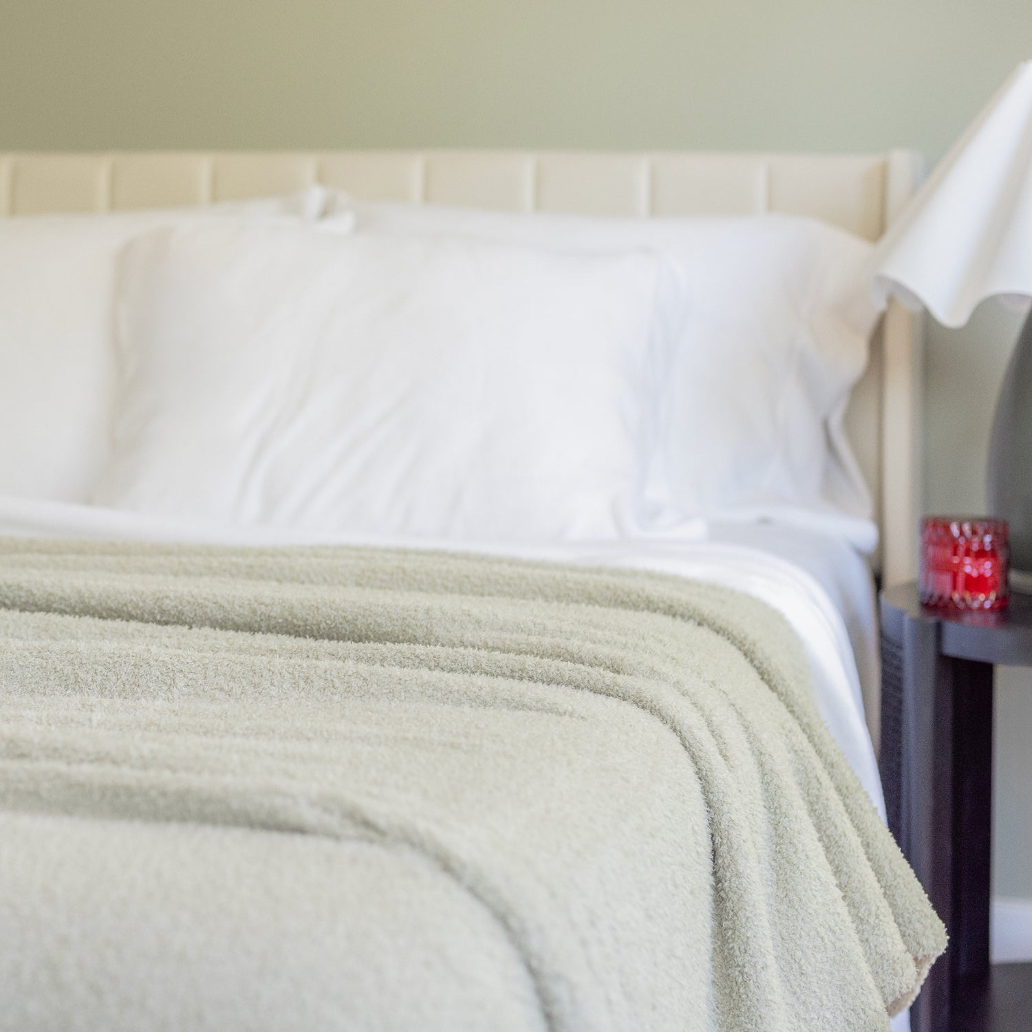 Bed with white bedding and a green blanket against a neutral wall.