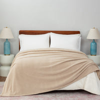 Beige blanket draped over a bed with white pillows and two lamps on nightstands.