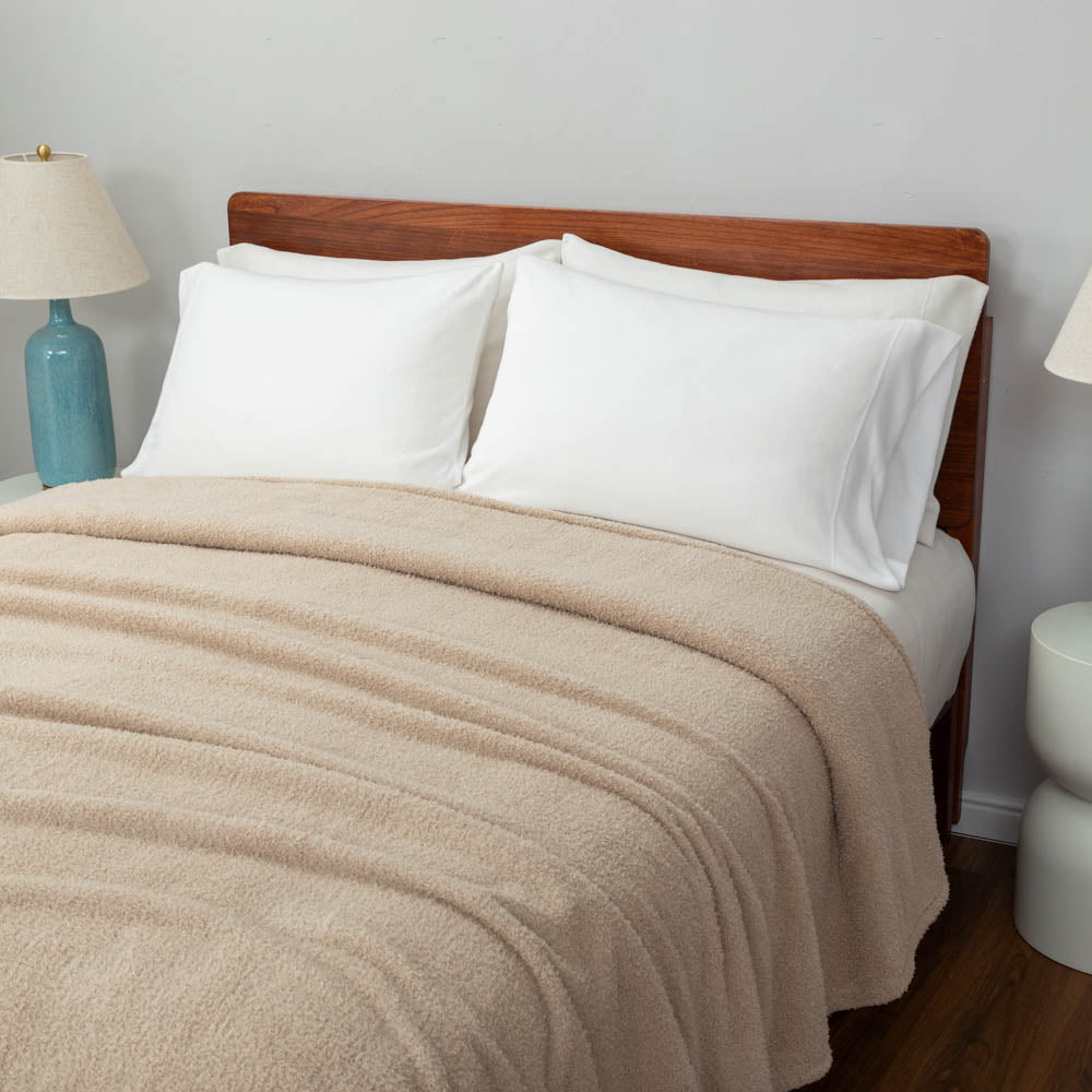 Beige blanket on a bed with white pillows and wooden headboard