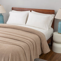 Bed with beige blanket, white pillows, wooden headboard, and side table with lamp.