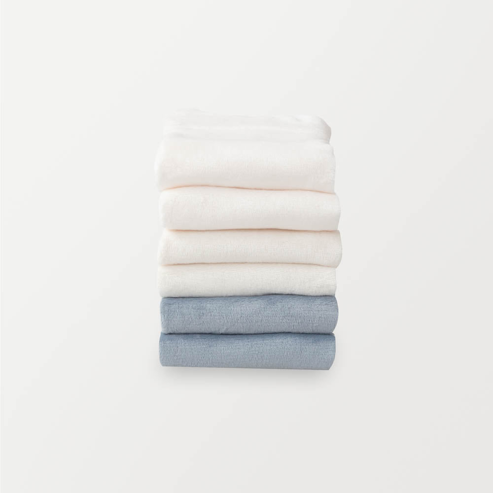 A stack of 6 pillowcases in white, cream, and blue folded neatly on a white surface.