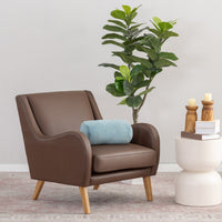 Brown armchair with a blue pillow next to a white side table with candles and books, against a light gray wall.