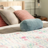 Bed with colorful bedding and a blue cylindrical pillow in a bedroom setting.