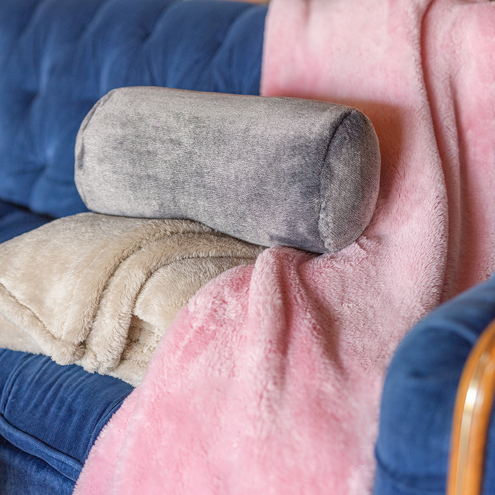 A grey neckroll pillow sitting on extra-fluffy throws.