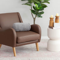 A grey EcoThread Neckroll Pillow sitting on a grey leather chair next to a table and plant.