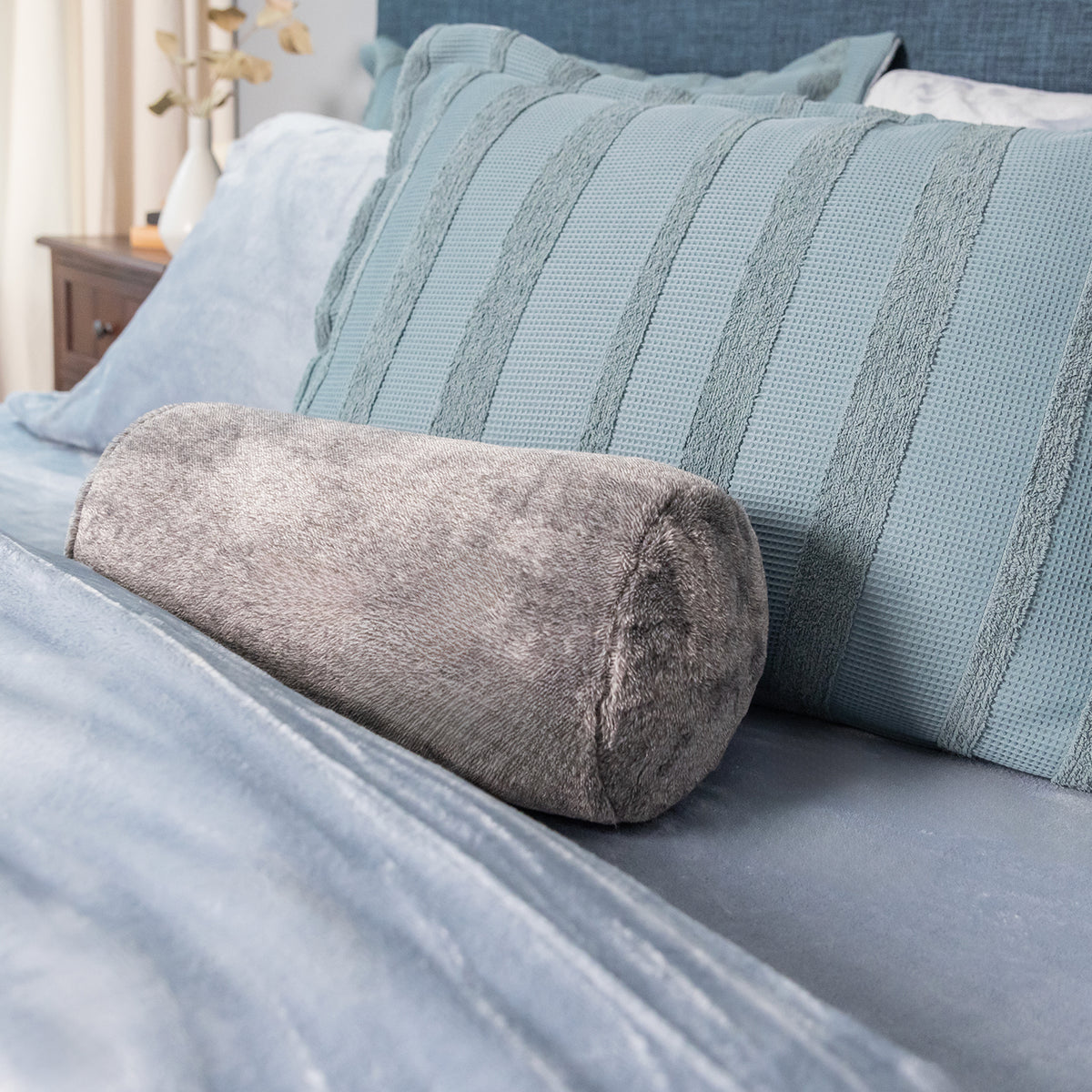 Grey neckroll pillow decorated on a blue bed.