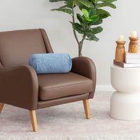 A blue EcoThread Neckroll Pillow sitting on a brown leather chair next to a table and plant.