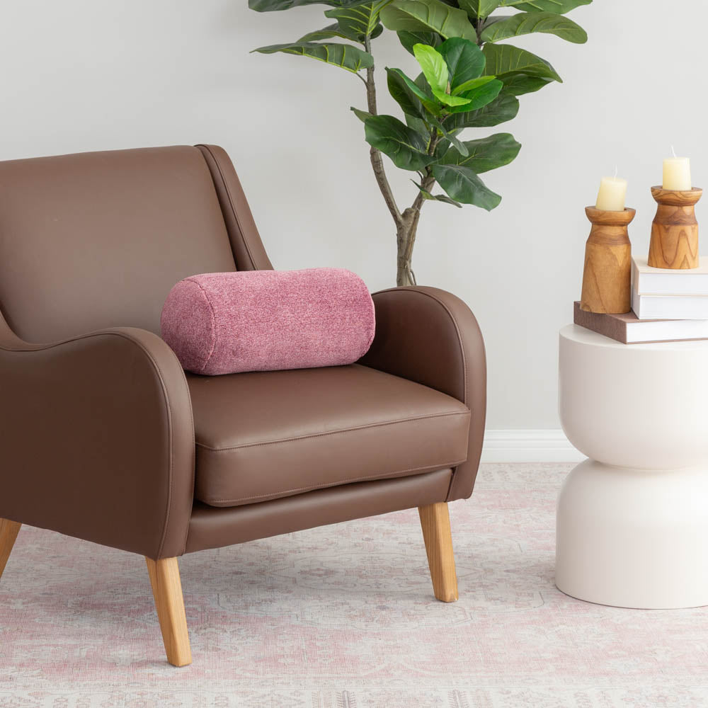A pink neckroll pillow sitting on a brown leather chair.