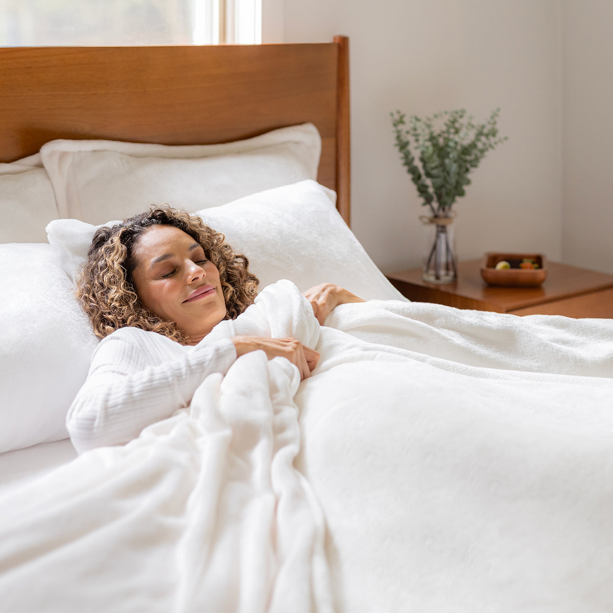 Woman lying in bed under white duvet in a bedroom setting
