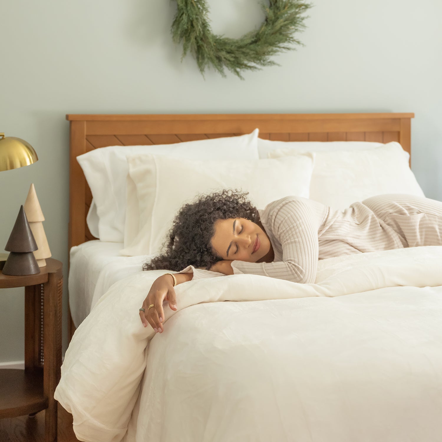 Woman sleeping in a bed with white bedding and wooden headboard, room decorated for Christmas.