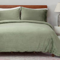 Green bedding set on a bed with a wooden headboard and lamp in the background.