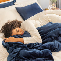 Woman sleeping under a blue blanket on a bed with white pillows.