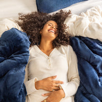 Woman lying on a bed with blue and white pillows and blankets, wearing a white shirt.