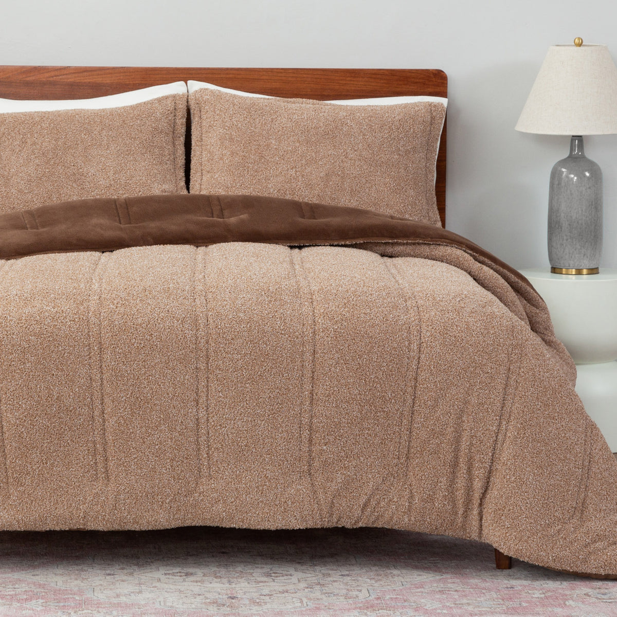 Beige and brown textured comforter on a bed with a wooden headboard and lamp in the background.
