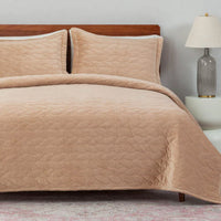 Beige quilted bedding set on a bed with a wooden headboard and lamp in the background.