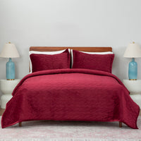 Red quilt set decorated on a bed in a neutral bedroom.