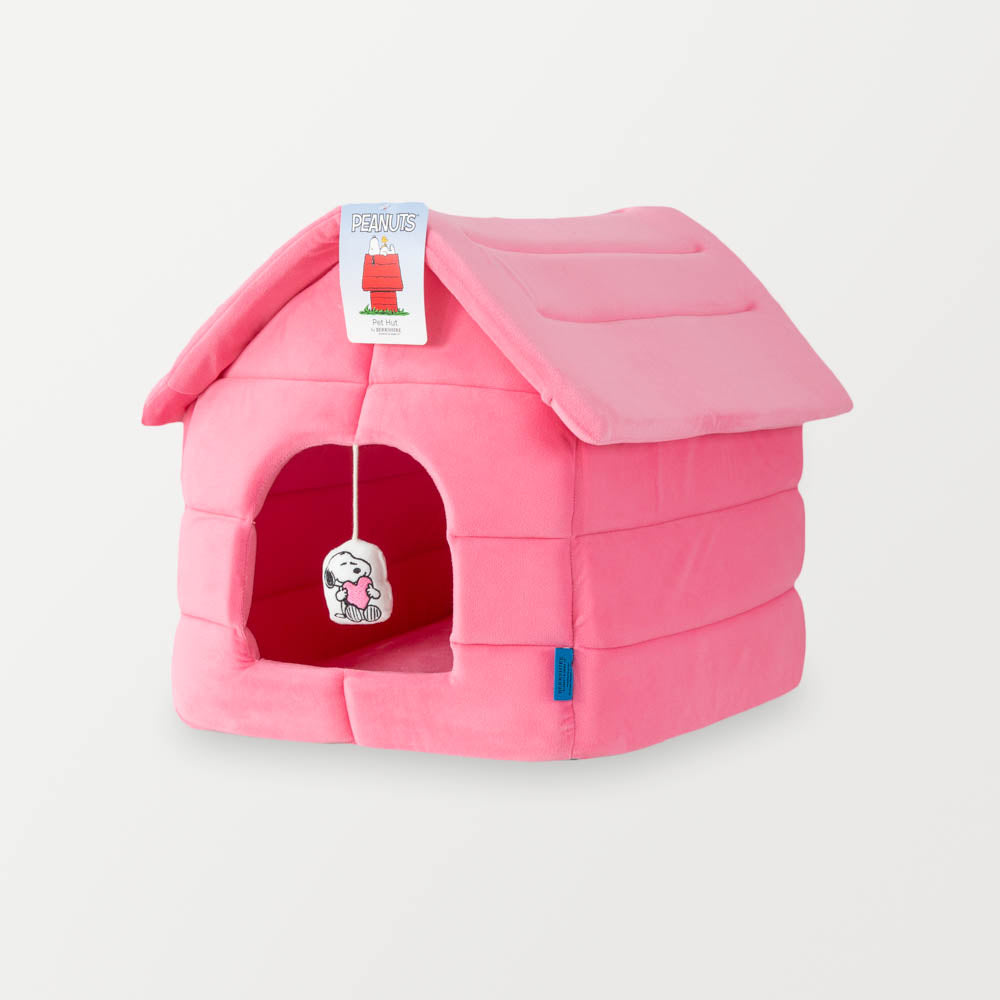 A pink snoopy dog house pet bed sitting on a white surface.