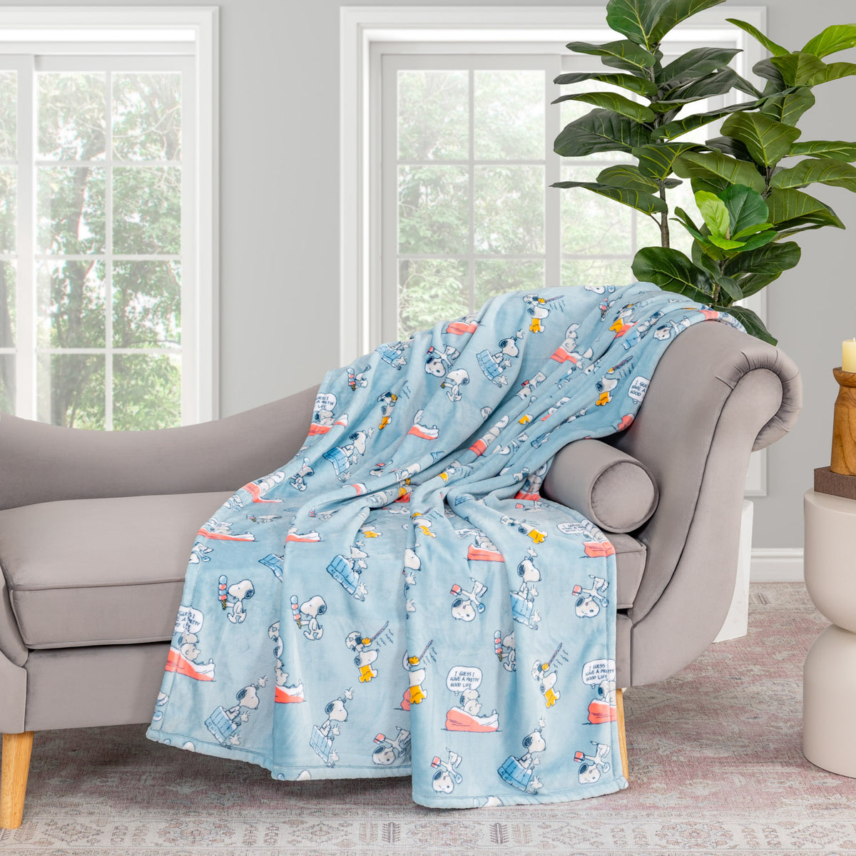 Blue Peanuts 75th Anniversary Throw draped neatly over a grey chair in a living space.