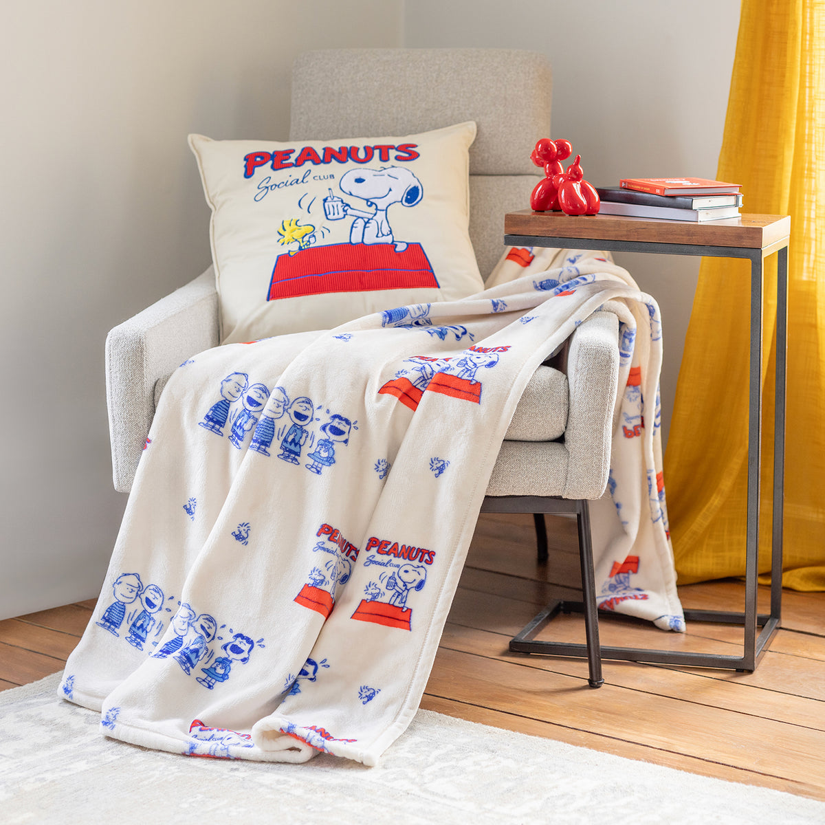 Peanuts social club throw and matching pillow decorated on a grey chair.